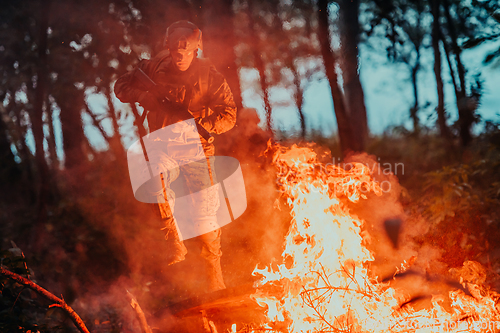 Image of Soldier in Action at Night in the Forest Area. Night Time Military Mission jumping over fire