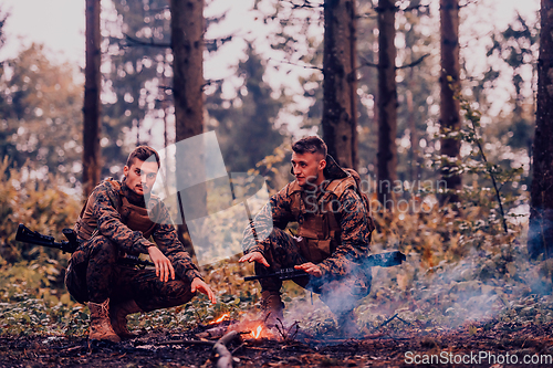 Image of Two exhausted soldiers sitting by the fire after a weary and heavy war battle