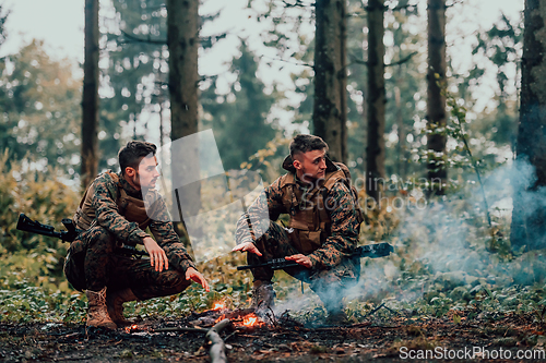 Image of Two exhausted soldiers sitting by the fire after a weary and heavy war battle