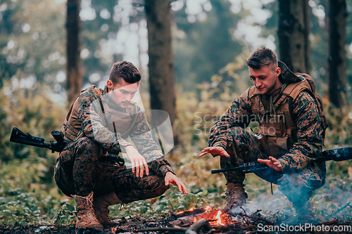 Image of Two exhausted soldiers sitting by the fire after a weary and heavy war battle