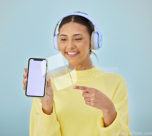 Image of Happy woman, phone mockup and pointing for advertising or marketing against a studio background. Female person smile and listening to music on headphones with mobile smartphone app display or screen