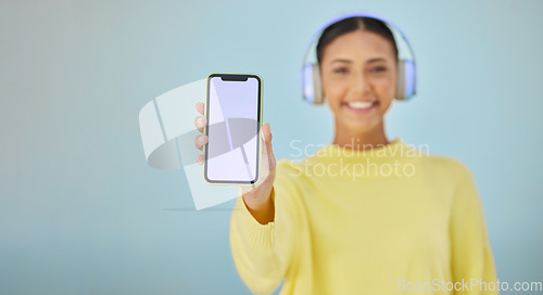 Image of Happy woman with phone screen, headphones and mockup in studio for social media post, mobile app and streaming radio. Smile, music media subscription and girl with cellphone on blue background space.