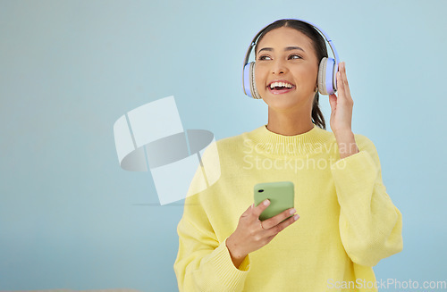 Image of Happy woman with phone, headphones and banner mockup in studio on social media, mobile app and streaming radio. Smile, relax and music media subscription, girl with cellphone on blue background space