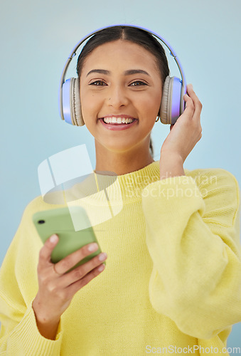 Image of Portrait of woman with phone, headphones and smile in studio for social media, mobile app and streaming radio site. Podcast, music media subscription and happy girl with cellphone on blue background.