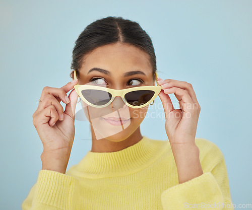 Image of Sunglasses, gen z and young woman in a studio with a casual, stylish and cool sweater outfit. Confident, face and female model with trendy style and fashion accessory isolated by a blue background.