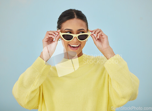 Image of Happy, sunglasses and young woman in a studio with a casual, stylish and cool sweater outfit. Happiness, smile and female model with trendy style and fashion accessory isolated by a blue background.
