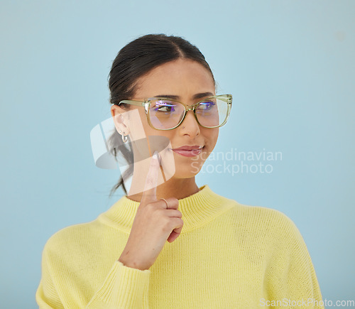 Image of Woman, smile and glasses in studio thinking, problem solving style and vision on blue background. Ideas, eyewear and happy model brainstorming with hand on face in cool fashion, mindfulness and gen z