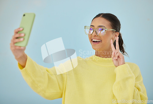 Image of Selfie, peace sign and happy studio woman with emoji v sign, icon and pose for social network, memory picture or photography. Gen z person, youth or influencer post to media app on blue background