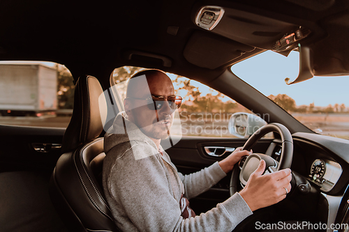 Image of A man with a sunglasses driving a car at sunset. The concept of car travel