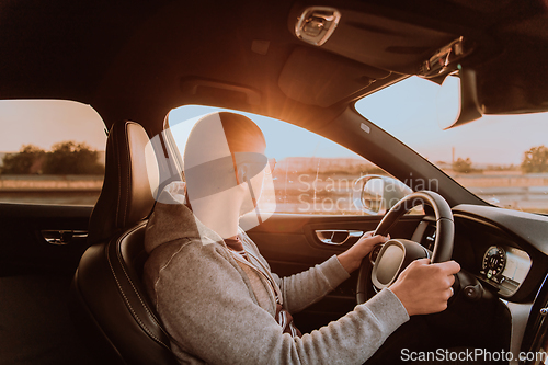 Image of A man with a sunglasses driving a car at sunset. The concept of car travel