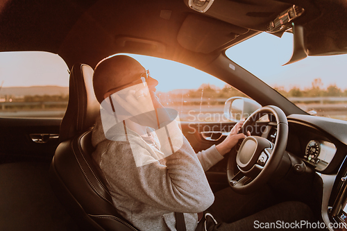 Image of A man with a sunglasses driving a car and talking on smartphone at sunset. The concept of car travel