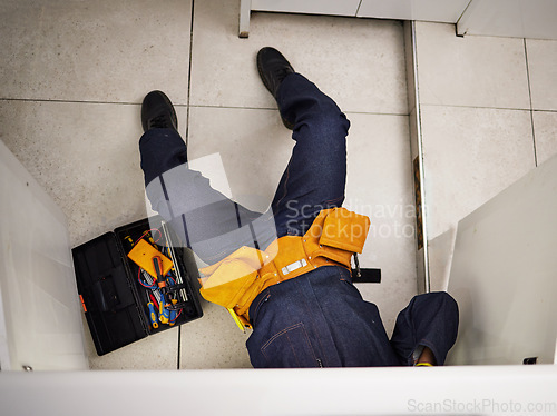 Image of Kitchen, maintenance and repair with a plumber on the floor of a home to fix a leak, issue or problem. Plumbing, renovation and tools with a handyman or contractor working on a pipeline in a house