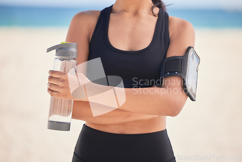 Image of Woman, fitness and water with arms crossed on beach for workout, exercise or natural outdoor nutrition. Hands of female person with bottle of mineral liquid for running, training or healthy wellness