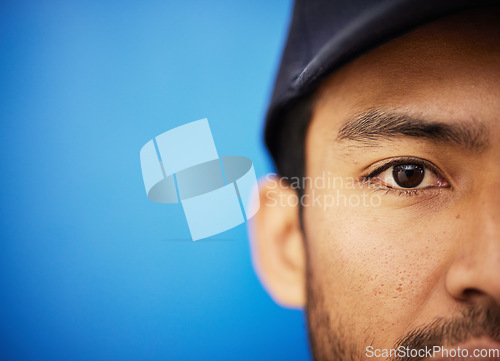 Image of Eye, closeup and portrait of half of man in sports on blue background with advertising, mockup or space with athlete in studio. Serious, face and Indian person in cricket or baseball cap and fitness