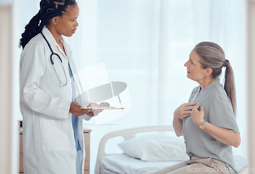 Image of Healthcare, consultation and doctor with senior patient in discussion on chest pain problem. Professional, clipboard and female medical worker talking to elderly woman with heart sickness in hospital