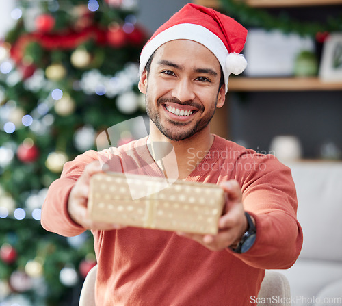Image of Christmas, portrait and asian man with gift giving in his home for celebration, fun and holiday with a smile. Happy, face and Japanese male with present box offer in a living room for festive event