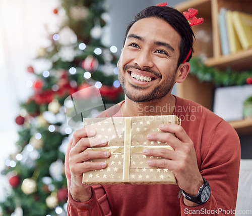 Image of Christmas, smile and asian man with gift in his home happy, excited and having fun holiday celebration. Hand holding, box and Japanese male with present in a living room at December party or event