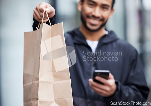 Image of Courier man, giving paper bag and portrait with phone, smile and delivery service in supply chain job. Young logistics worker, package and hand with smartphone, product and e commerce in metro cbd