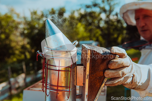 Image of The beekeeper using smoke to calm the bees and begins to inspect the honey