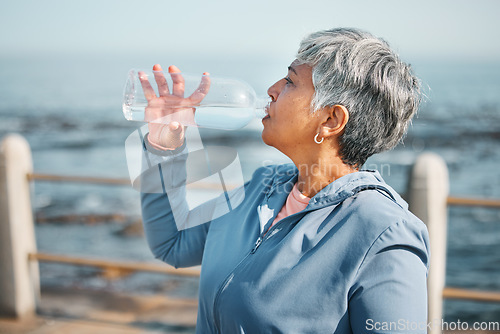 Image of Outdoor, fitness or senior woman drinking water for hydration, wellness and thirsty on beach run, training or exercise. Bottle, runner or elderly person refresh with cold liquid on retirement workout