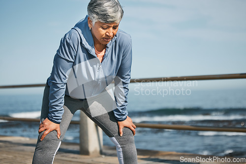 Image of Senior, exercise and tired woman at the beach on break from training, workout or morning cardio run in nature. Sports, fatigue and elderly female runner stop to breathe on ocean workout or fitness