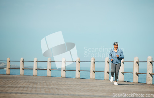 Image of Fitness, running and senior woman at the beach for exercise, health or cardio on blue sky background. Training, wellness and elderly female runner at the sea for morning workout, routine or ocean run