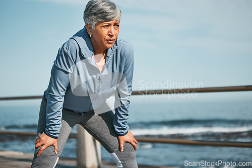 Image of Senior, fitness and tired woman at the beach on break from training, workout or morning cardio run in nature. Sports, fatigue and elderly female runner stop to breathe on ocean workout or performance