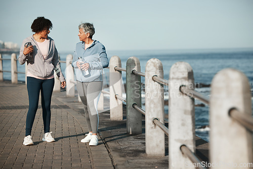 Image of Fitness, walking and women by ocean talking for healthy lifestyle, wellness and cardio on promenade. Sports, friends and female people in conversation on boardwalk for exercise, training and workout