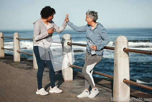 Image of Fitness, high five and senior women by ocean for healthy lifestyle, wellness and cardio on promenade. Sports, friends and female people celebrate on boardwalk for exercise, training and workout goals