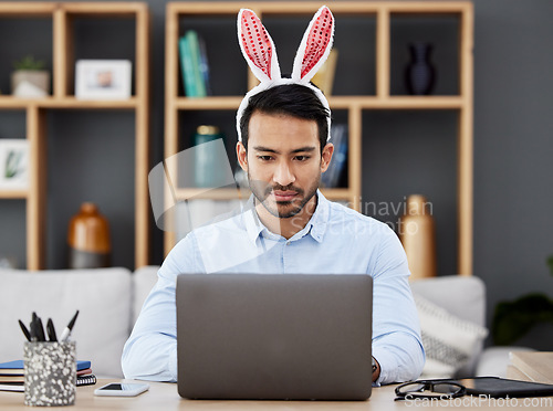 Image of Laptop, bunny ears and business man for Easter in office with decoration for celebration, event and party. Corporate, focus and Asian male person on computer at desk with rabbit headband for holiday