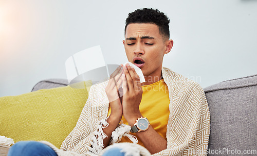 Image of Sick, couch and man with flu sneeze due to cold, sinus and fever in a home living room with a blanket on a sofa. Healthcare, sad and young person with difficult symptoms or medical problem in house