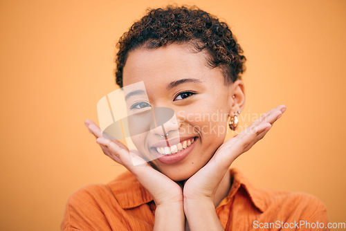 Image of Happy, woman and hands on face in studio with smile and confidence feeling cute. Orange background, young portrait and African female person with trendy, modern and student fashion of gen z glow