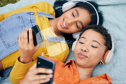 Image of Headphones, phone and lgbt couple on picnic on grass, relax, technology and streaming service in nature. Cellphone, listening to music and happy lesbian women on blanket in garden together from above