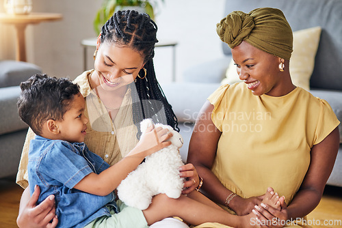 Image of Happy, gay family and child with a teddy bear on a home floor for development, fun and smile. Adoption, lesbian or LGBT women or parents and kid together in a lounge while playing with toys to relax