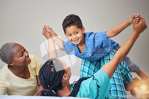 Image of Child, gay family and playing on bed in home bedroom for security, quality time and love. Adoption, lesbian or LGBTQ women or parents lift a happy kid to wake up with care, fun game and a smile