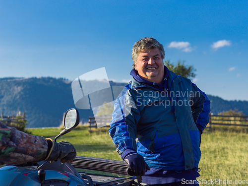 Image of A man in a forest posing next to a quad and preparing for ride