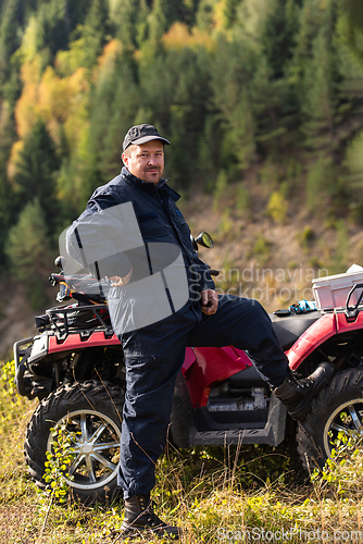 Image of A man in a forest area posing next to a quad and preparing for ride
