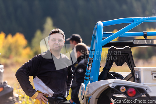 Image of A man in a forest posing next to a quad and preparing for ride