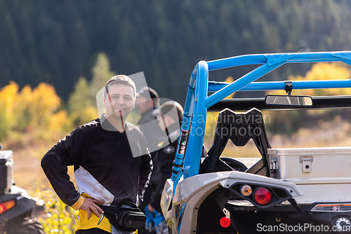 Image of A man in a forest posing next to a quad and preparing for ride