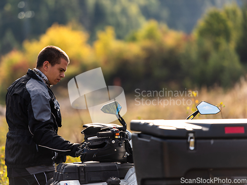 Image of A man in a forest posing next to a quad and preparing for ride