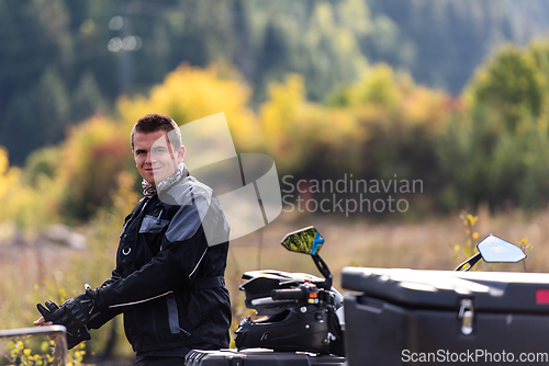 Image of A man in a forest posing next to a quad and preparing for ride