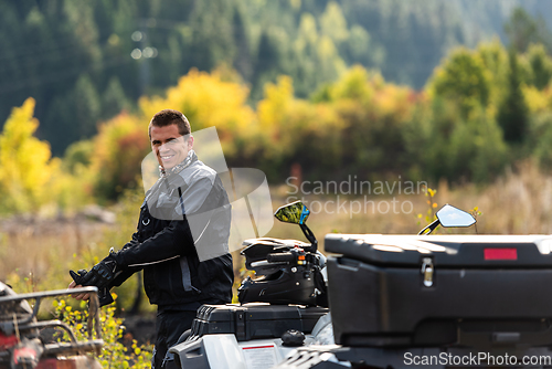 Image of A man in a forest posing next to a quad and preparing for ride