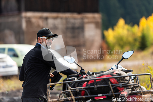 Image of A man in a forest posing next to a quad and preparing for ride