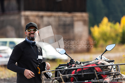 Image of A man in a forest posing next to a quad and preparing for ride