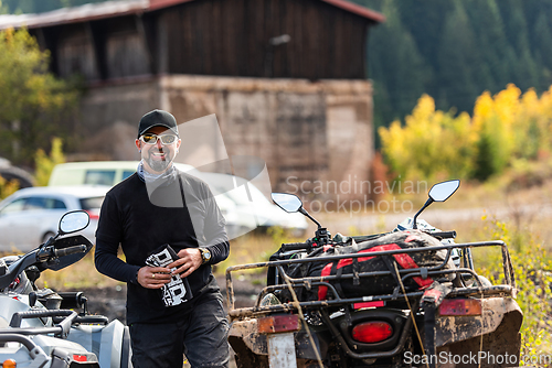 Image of A man in a forest posing next to a quad and preparing for ride