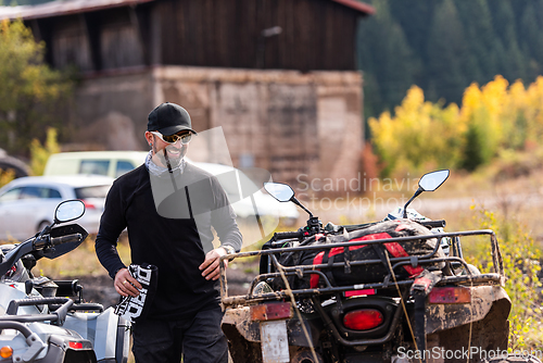 Image of A man in a forest posing next to a quad and preparing for ride