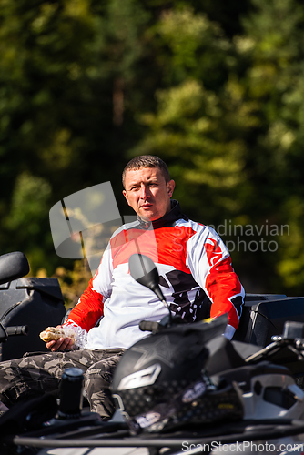 Image of A man in a forest posing next to a quad and preparing for ride