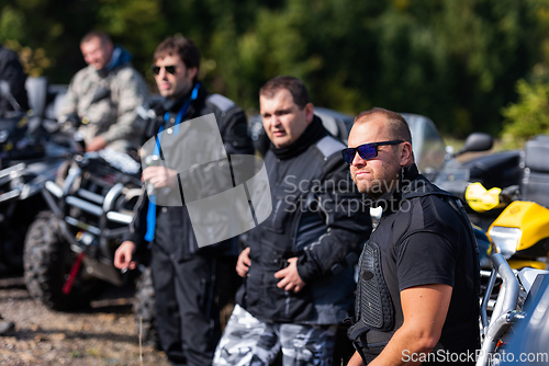 Image of A group of men on a social gathering are preparing to ride an ATV quad bike. People Ride together on a quad atv on muddy forest roads