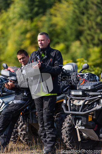 Image of A group of men on a social gathering are preparing to ride an ATV quad bike. People Ride together on a quad atv on muddy forest roads