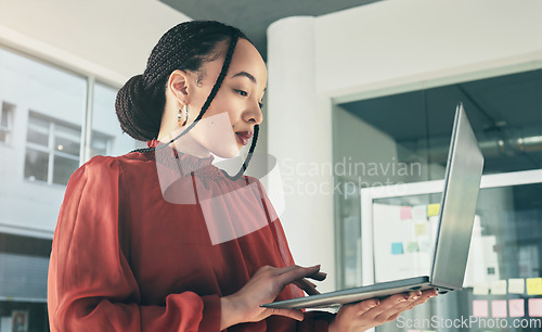 Image of Woman standing in office with laptop, research and ideas on website for business plan, brainstorming or proposal process. Thinking, typing and businesswoman on computer with online review at startup.